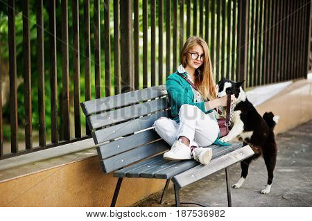 Trendy Girl At Glasses And Ripped Jeans With Russo-european Laika (husky) Dog On A Leash, Against Be