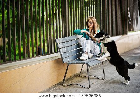 Trendy Girl At Glasses And Ripped Jeans With Russo-european Laika (husky) Dog On A Leash, Against Be