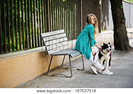 Trendy Girl At Glasses And Ripped Jeans With Russo-european Laika (husky) Dog On A Leash, Against Be