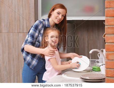 Little girl and her mother doing the washing-up in kitchen at home