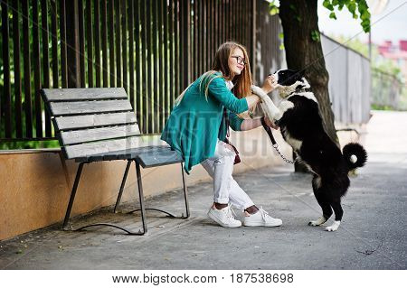 Trendy Girl At Glasses And Ripped Jeans With Russo-european Laika (husky) Dog On A Leash, Against Be