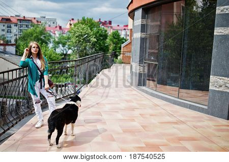 Trendy Girl At Glasses And Ripped Jeans With Russo-european Laika (husky) Dog On A Leash, Against Bu