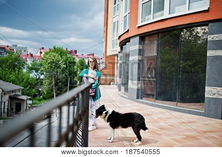 Trendy Girl At Glasses And Ripped Jeans With Russo-european Laika (husky) Dog On A Leash, Against Bu