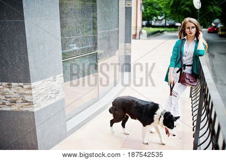 Trendy Girl At Glasses And Ripped Jeans With Russo-european Laika (husky) Dog On A Leash, Against Bu