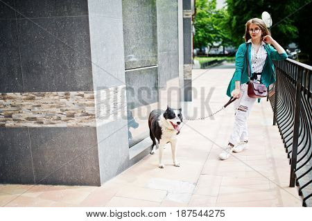 Trendy Girl At Glasses And Ripped Jeans With Russo-european Laika (husky) Dog On A Leash, Against Bu