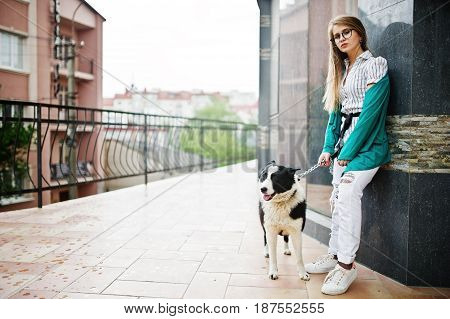 Trendy Girl At Glasses And Ripped Jeans With Russo-european Laika (husky) Dog On A Leash, Against St