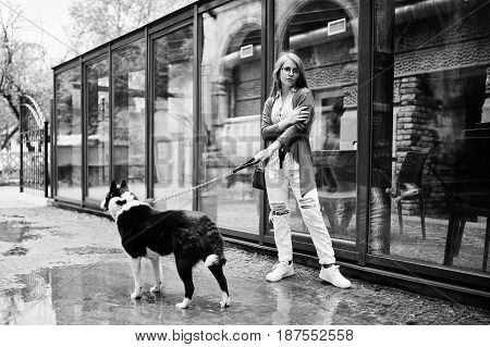 Trendy Girl At Glasses And Ripped Jeans With Russo-european Laika (husky) Dog On A Leash, Against St