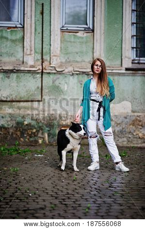 Trendy Girl At Glasses And Ripped Jeans With Russo-european Laika (husky) Dog On A Leash, Against St