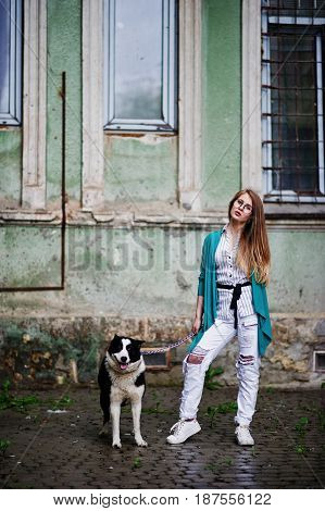 Trendy Girl At Glasses And Ripped Jeans With Russo-european Laika (husky) Dog On A Leash, Against St