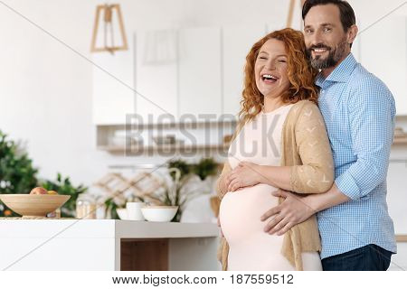 True love. Mature couple waiting for a baby laughing out loud while posing together and looking at the camera.