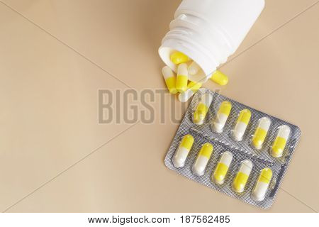 Yellow medicine capsules. Pills blister pack and tablets bottle on beige background