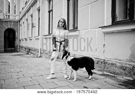 Trendy Girl At Glasses And Ripped Jeans With Russo-european Laika (husky) Dog On A Leash, Against St