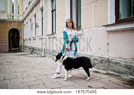 Trendy Girl At Glasses And Ripped Jeans With Russo-european Laika (husky) Dog On A Leash, Against St