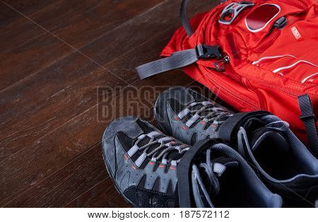 Hiking equipment: backpack and trekking boots on the wooden boards. Horizontal photo and brown background. Tourist backgrounds and still-life. Preparation and planning for the travelling. Concept of the active lifestyle.