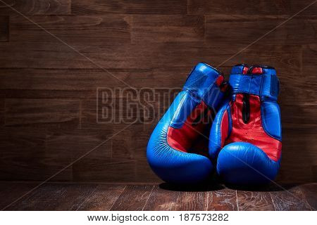 Boxing background with two gloves on the brown plank background. Horizontal photo of the blue and red boxing gloves against wooden wall. Boxing training and exercise. Concept of the sportive lifestyle.