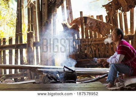 MAE KLANG LUANG, THAILAND, FEBRUARY 2, 2017 : A Karen tribe man is sitting and smoking a cigarette, waiting for the tea water to boil in the village of Mae Klang luang near Chiang Mai, Thailand