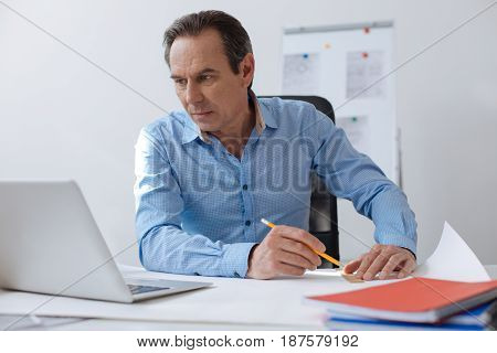 Implement your ideas. Pleasant professional engineer sitting at the table and drawign blueprint while sitting in the office
