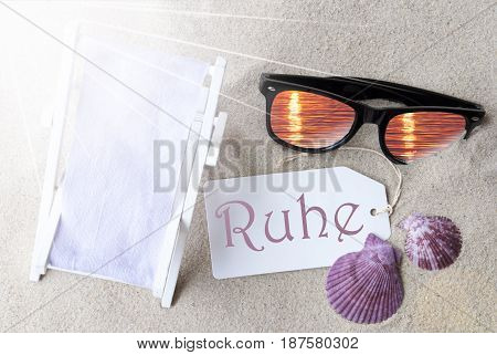 Sunny Summer Label With German Text Ruhe Means Peace. Flat Lay View. Summer Decoration With Deck Chair, Seashells And Sunglasses. Greeting Crad With Sand Background