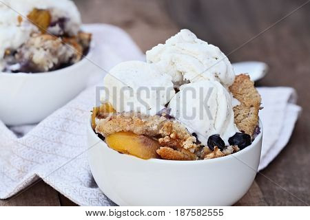 Fresh peach and blueberry cobbler served with vanilla ice cream. Shallow depth of field with selective focus.