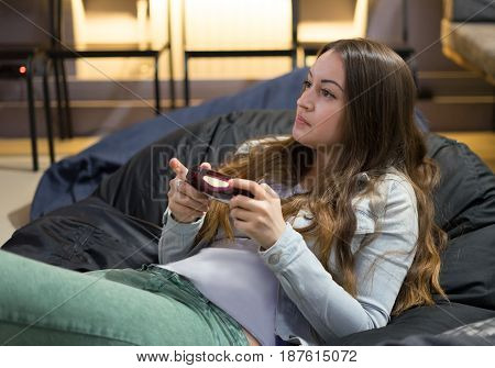 gamer girl playing video games with joystick sitting on Bean bag chair.