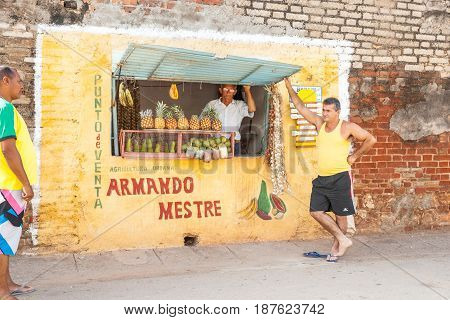 Trinidad, Cuba -July 2, 2012; Hole in wall fruit shop with Spanish sign vendor behind fruit display man standing casually in Trinidad de Cuba.