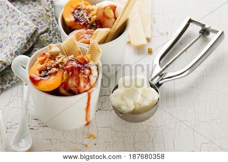 Tasty fresh cold appetizing vanilla ice cream with nuts apricots waffles and syrup on white table with ingredients for making dessert. Closeup.