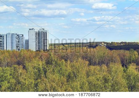 View of the high panel dwelling houses standing against a lonely church surrounded by dense forest