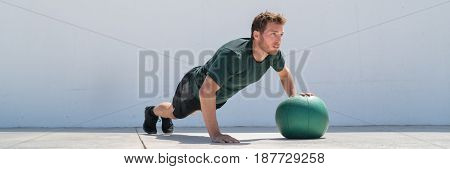 Fitness man banner crop. Athlete strength training pushup chest and shoulder muscles doing alternating single arm medicine ball push-ups floor exercises at outdoor gym.