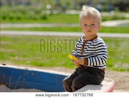 Portrait of toddler child outdoors. One year old baby boy playing with sand at playground sandbox