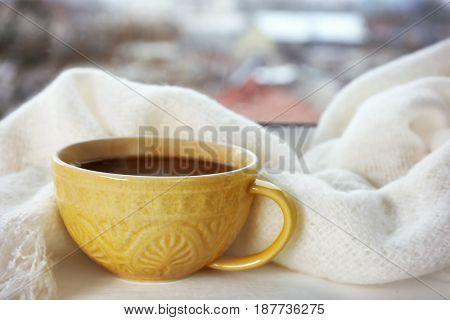 Patterned cup of hot tasty drink and fluffy scarf on windowsill