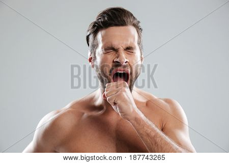 Portrait of a handsome bored beraded man with naked shoulders yawning isolated over white background