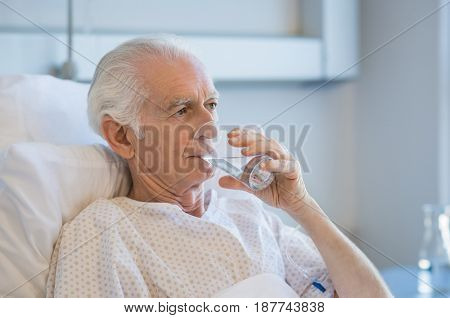 Senior patient in hospital drinking water. Old man recovering from disease in hospital drinking water after taking medicine. Aged man admitted to hospital resting on bed.