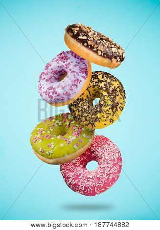 Tasty doughnuts in motion falling on pastel blue background, close-up.
