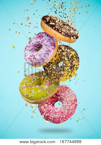 Tasty doughnuts in motion falling on pastel blue background, close-up.