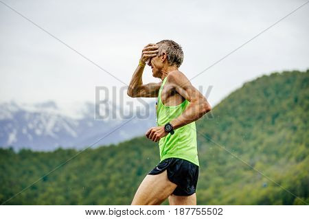 Rosa Khutor Russia - May 7 2017: old man runner on water point in hand sponge with water in race Spring mountain marathon