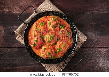 An overhead photo of meatballs in tomato sauce, shot from above in the skillet on dark rustic textures, with a place for text