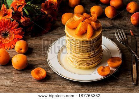 Stack of homemade american pancakes served with honey and apricots on wooden background.