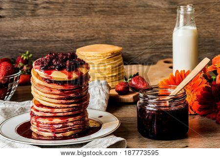Stack of homemade american pancakes served with jam and strawberries on wooden background.