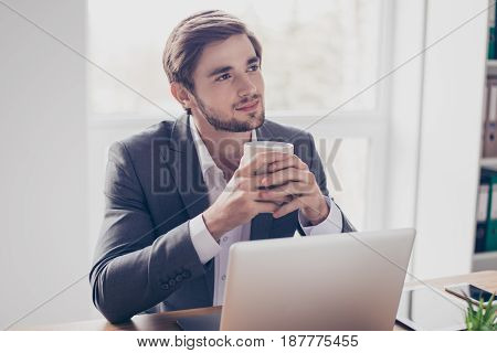 Young Dreaming Worker Is Thinking In Front Of Laptop At Work Place. He Is Happy, Smiling And Holding