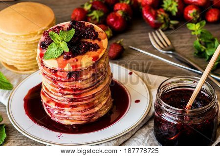 Stack of homemade american pancakes served with jam and strawberries on wooden background.