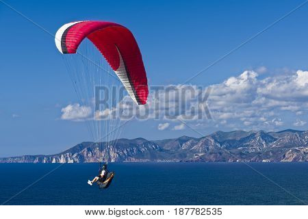 Colorful hang glider in sky over blue sea. Sardinia South West
