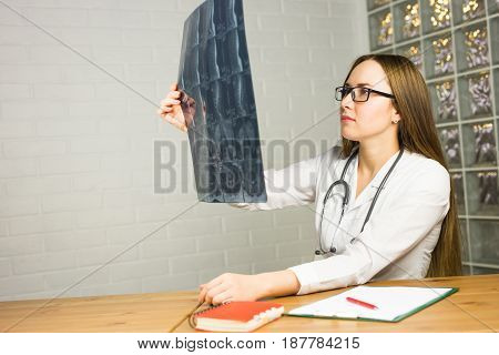 Portrait of intellectual woman healthcare personnel with white labcoat, looking at full body x-ray radiographic image, hospital clinic background. Radiology department.