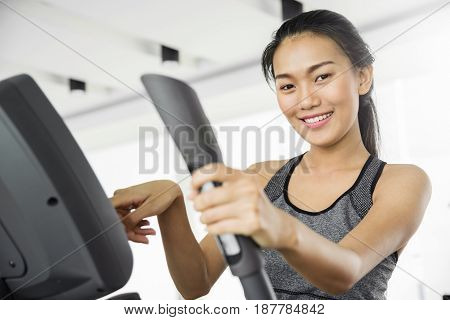 Asian woman smling and using Elliptical trainer machine at the gym.