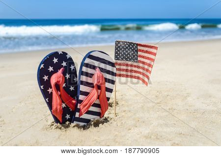 Patriotic USA background with flip flops and American flag on the sandy beach