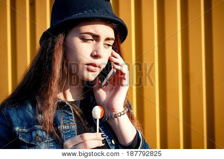 Stylish Young Girl In Hat, Skirt Shoes And Denim Jacket With Candy On Stick, Chupa Chups, On Sunny D