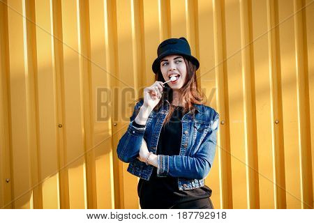 Cheerful Stylish Young Girl In Hat, And Jeans Jacket With Candy On Stick, Chupa Chups, On Sunny Day