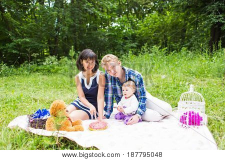 Happy young mother and father with their baby daughter relaxing on a blanket in a park celebrating with birthday cake.