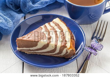 Delicious homemade chocolate cake with cottage cheese Zebra (Marble cake). Tasty breakfast. Piece of cake on blue plate blue cup and blue gauze textiles on white wooden table. Selective focus