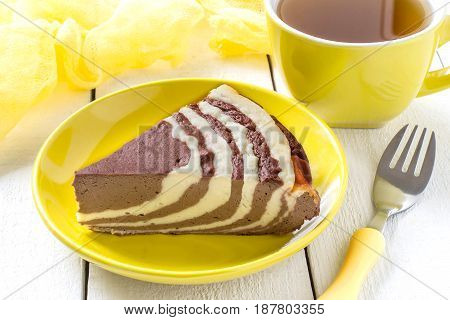 Delicious homemade chocolate cake with cottage cheese Zebra (Marble cake). Tasty breakfast. Piece is cut from cake yellow cup of tea and yellow gauze textiles on white wooden table. Selective focus
