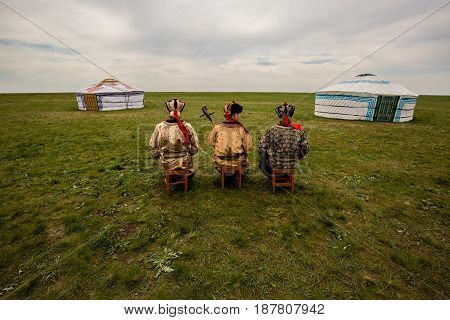 Three Kalmyk musicians in national costumes in the steppe against the background of yurts, the spring steppe. Russia